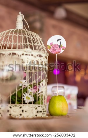 Wedding table decoration, cage bird in focus, number seven stabbed in apple.