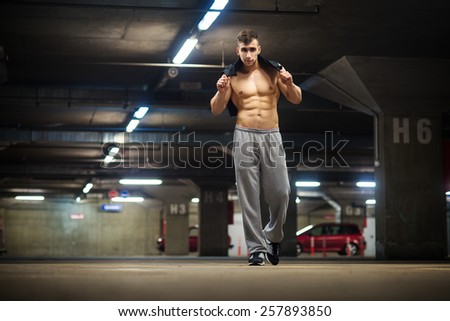 Handsome muscular young man posing at parking garage, natural lights, dark place.