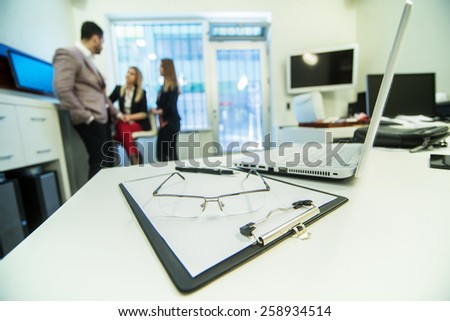 Close-up of workplace in modern office with business people blurred in background.