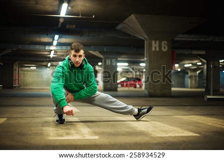 Handsome athlete stretching at parking garage. Natural lights, dark place.