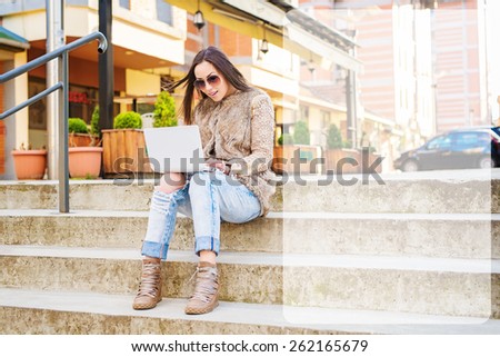 Beautiful young woman sitting on stairs, holding lap top and typing. Empty text box on the right side. Shallow depth of field.