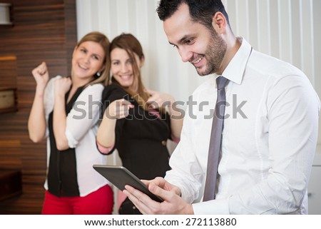 Successful businessman with tablet at office. Two female colleague rejoice in background.