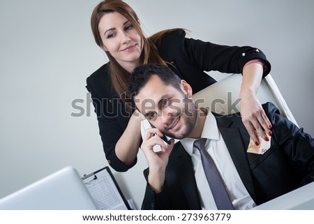 Female business woman giving money to businessman. Putting money him in the pocket while he is talking on the phone.