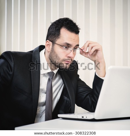 Handsome businessman sitting at office and looking at laptop. Business, office, marketing and sale concept. Satisfied businessman.