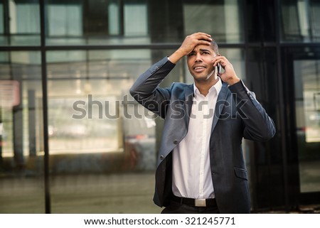Handsome businessman standing at street, talking on a mobile phone and having bad conversation.