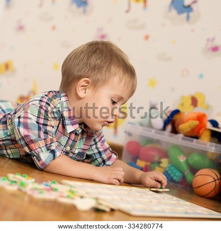 Adorable kid playing in a room with his toys. He is young designer with many ideas waiting to be found. Very shallow depth of field.