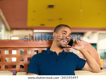 Handsome black man sitting at cafe bar and talking on mobile phone. He is looking aside and smiling.