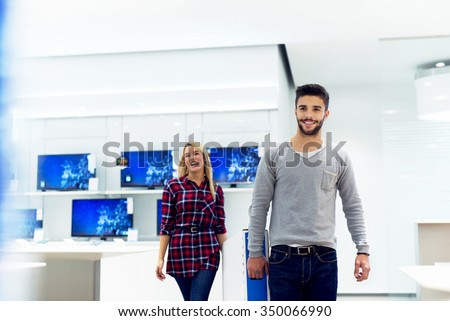 Couple in shopping at TV store. They are walking and holding big unpacked tv. Shallow depth of field. Selective focus on him.