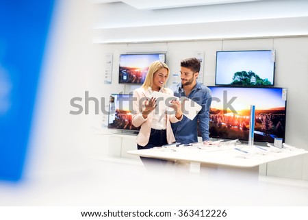 Lovely couple is at store and they are looking for a new mobile, tablet or TV at catalog. Shallow depth of field.