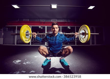 Handsome weightlifter at gym doing squats.