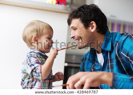 Father and son having a good time. Kid is painting father\'s face with watercolors. Shallow depth of field.