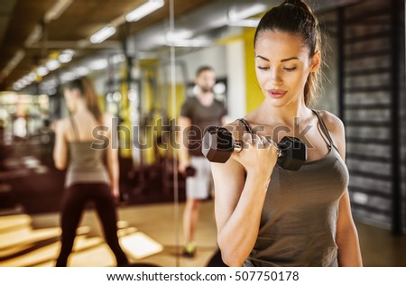 Attractive young woman working out with dumbbells at a gym.