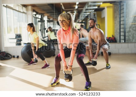Healthy young athletes doing exercises with kettlebells, at fitness studio.