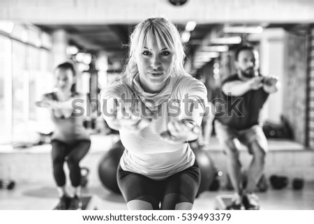 Group of athletes doing squats at gym. Black and white.