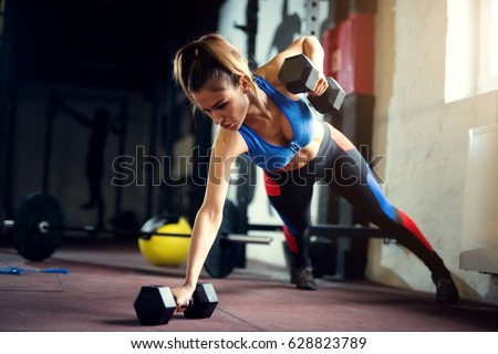 Female hard work at gym with dumbbells push ups. Strong woman at gym.