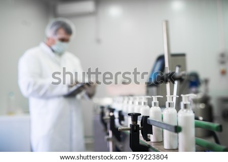 Close up of liquid soap going on a production line in front of cosmetics fabric worker typing on a tablet.