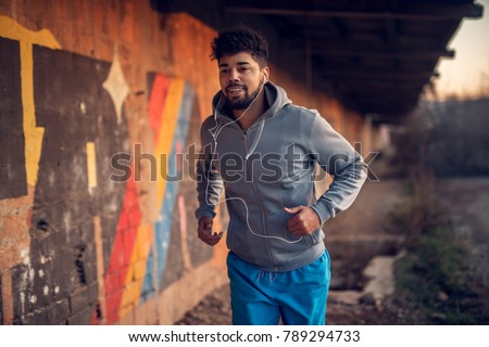 Portrait of happy afro-american attractive active runner man jogging outside on abandon place with earphones.