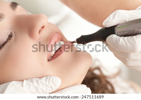 Healthy Spa: Young Beautiful Woman Having Permanent Make-up (Tattoo) on her Lips . Close-up .