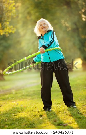 Healthy Senior  Woman doing Exercises with the Plastic Hoop at the Green Meadow in the Bright Autumn Evening