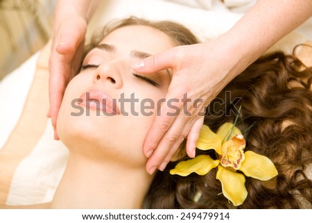Healthy spa: young beautiful relaxing woman having a facial massage, with orchid in long brown hair