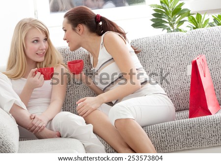 Two Young Beautiful Women Sitting on the Sofa, Drinking Tea and Talking Together