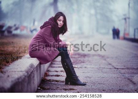 Disappointing Young Woman is Sitting in Depression on the Stone Parapet in the Gloomy Autumn Day