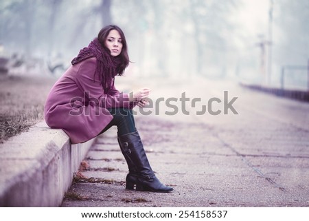 Disappointing Young Woman is Sitting in Depression on the Stone Parapet in the Gloomy Autumn Day