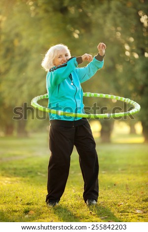 Seventy years old Senior Woman doing Exercises with Plastic Hoop Outdoors in the Bright Autumn Evening