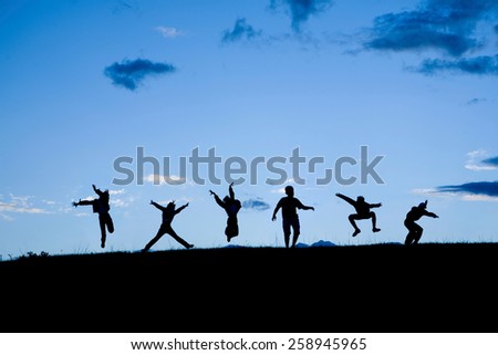 Black silhouettes of six people jumping together at the blue sky at the sunset