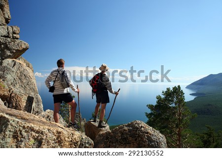 Two tourists are admiring the beautiful view from the mountain on the Baikal lake.