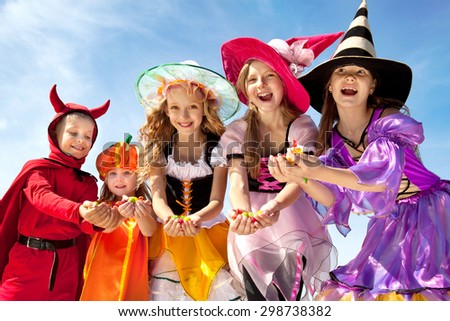 Five Happy Children Holding Candies in Halloween Costumes of Witches, Pumpkin and Devil at the Blue Sky