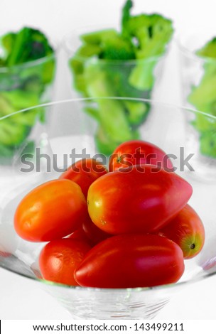 A close up grape tomato on a glass background with green broccoli
