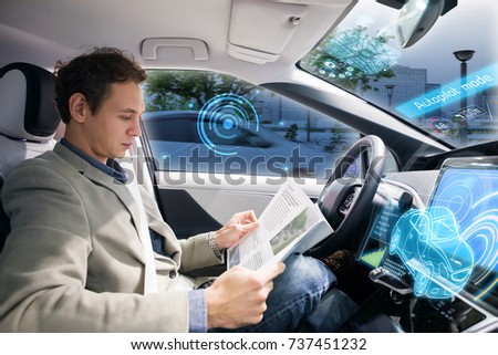 Caucasian driver reading magazine in autonomous car. Self driving vehicle.
