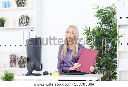Young blond  businesswoman with folder sits at the table at the office