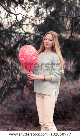 Open portrait of the young woman the beautiful woman in cold weather in park. The sensual blonde poses and is cheerful with a red balloon.