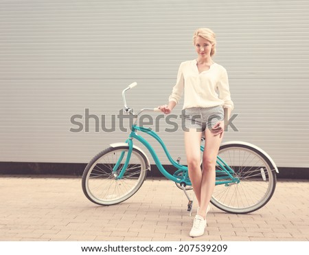 Beautiful blonde girl is standing near the vintage bicycle have fun and good mood looking in camera and smiling