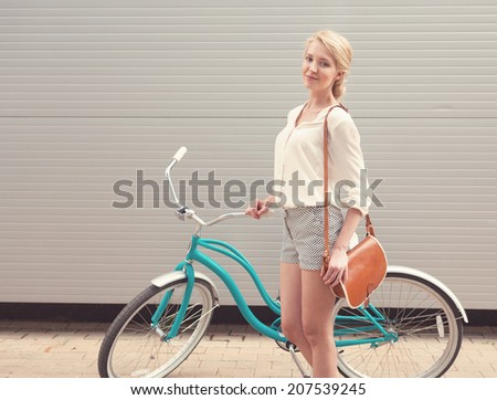Beautiful blonde girl is standing near the vintage bicycle with brown vintage bag
