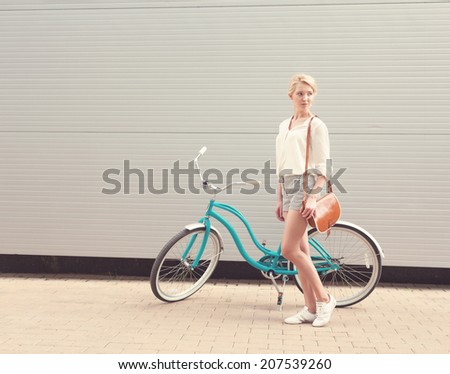 Beautiful blonde girl is standing near the vintage bicycle with brown vintage bag