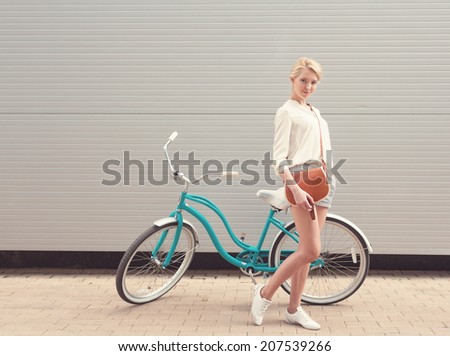 Beautiful blonde girl is standing near the vintage bicycle with brown vintage bag have fun and good mood looking in camera and smiling