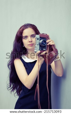 Beautiful brunette with long hair looking at the camera and holding in hands vintage camera