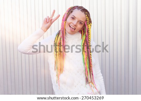 Beautiful girl with dreadlocks sunny summer afternoon shows victory sign fun posing near the wall