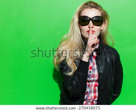 Beautiful blond girl  summer sunny day in the black jacket and lips finger asking for silence