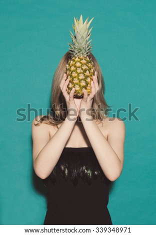Pineapple girl holds hands covering her own face in a black dress on a green background in the studio. Concept. Fashion Beauty Girl. Hairstyle. Make up. Sexy Glamour Girl