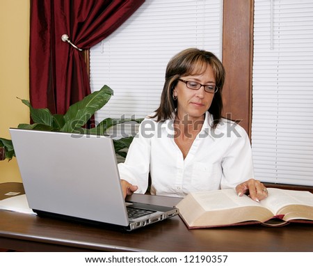a woman doing business research in large books and typing on the laptop