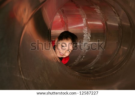 young male child playing sliding in a metal tube slide on a playground