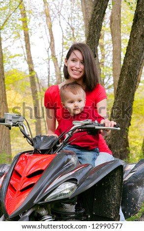 adult female and young male child riding on a four wheel all terrain vehicle in the woods