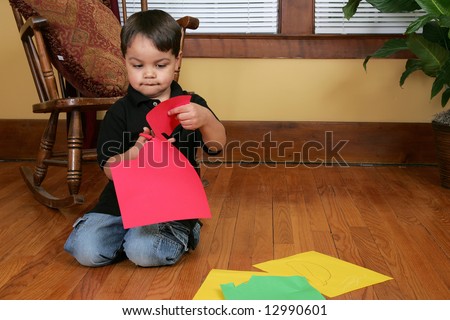 a young male child cutting paper strips on the floor