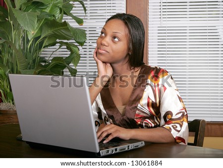 African American female adult working at a laptop computer and thinking