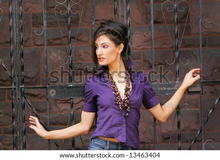 beautiful fashion female model holding onto a wrought iron gate and posing