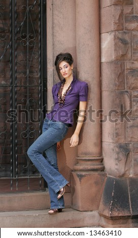 beautiful fashion female model leaning into a column near a wrought iron gate and posing